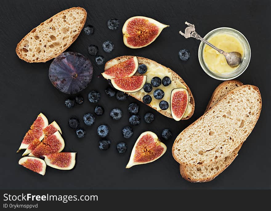 Fresh homemade bread, homemade baking. Blank for sandwich, figs, blueberries, sauce. Top view. Black stone background.