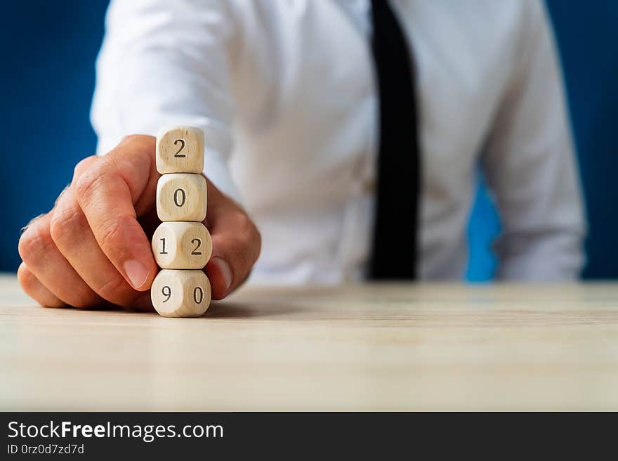 Businessman holding a stack of wooden dices carrying a 2019 sign turning in to 202. Over navy blue background. Businessman holding a stack of wooden dices carrying a 2019 sign turning in to 202. Over navy blue background