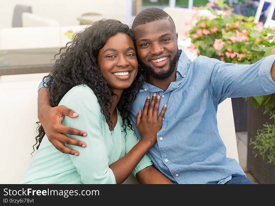 Young African Couple Hugging And Sitting In Cafe Doing Selfie