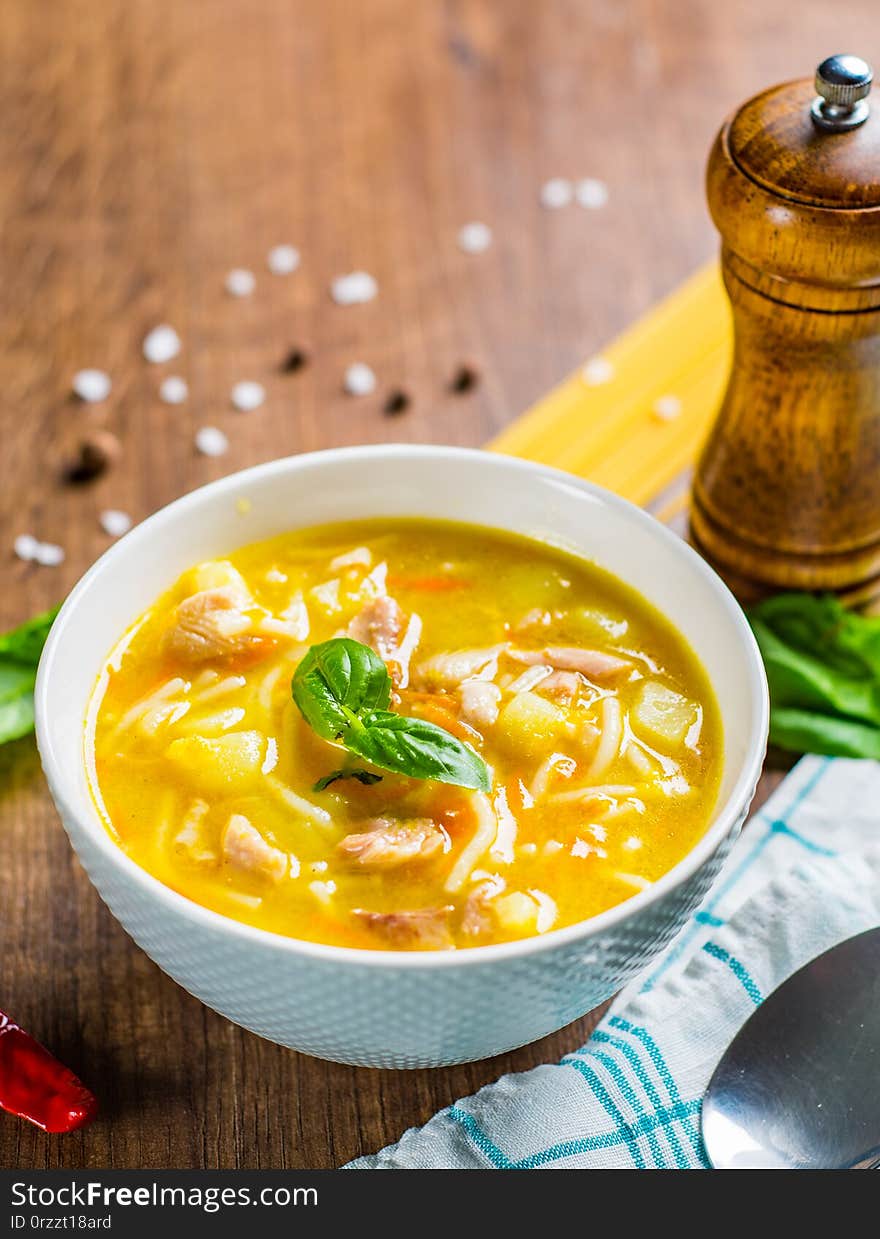 Chicken soup with noodles and vegetables in white bowl on wooden table