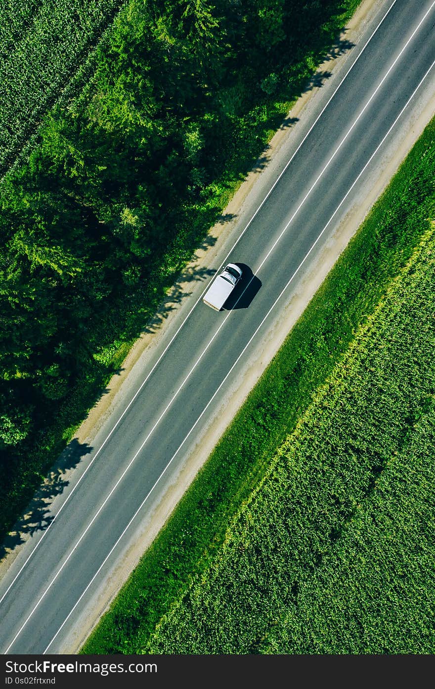 Aerial top view of a rural asphalt road through a green corn field in summer
