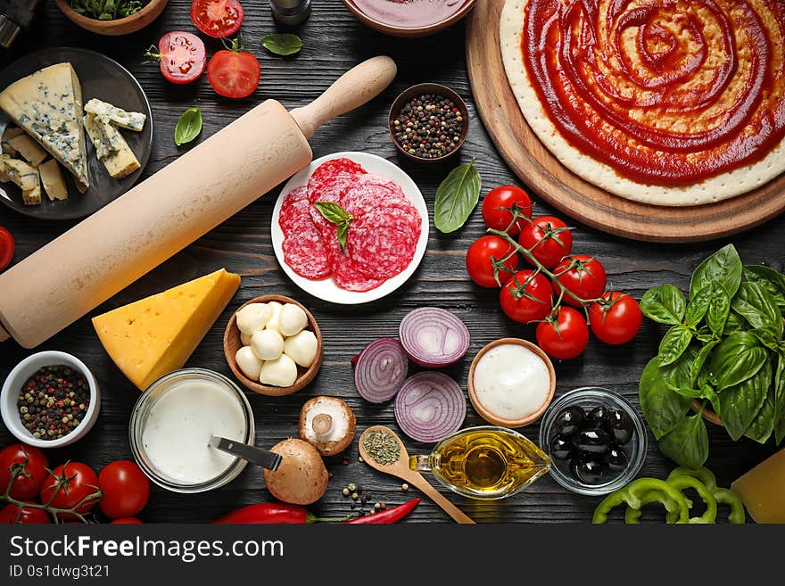 Flat lay composition with pizza crust and ingredients on dark wooden table