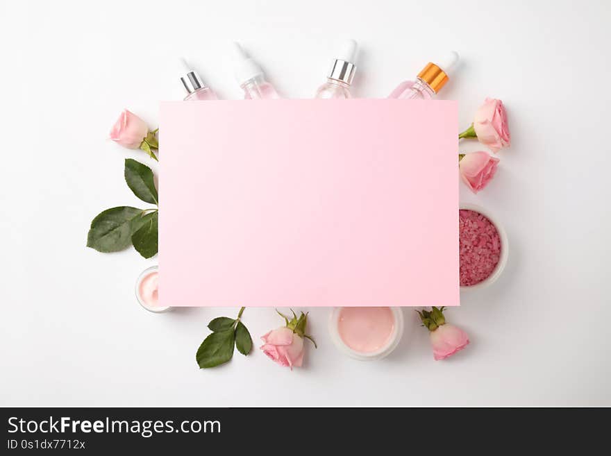 Composition with rose essential oil and blank card on white background, top view.