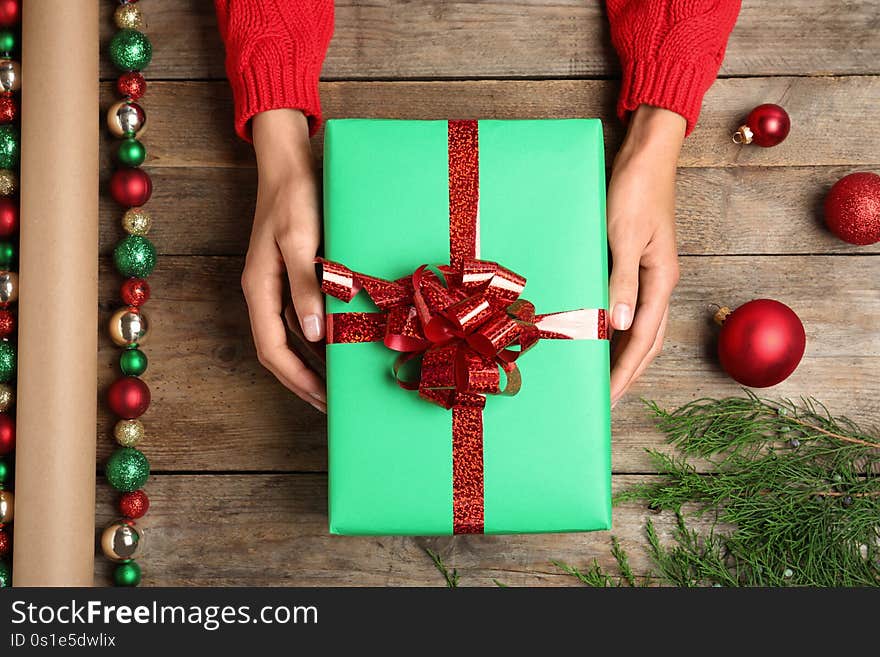 Woman wrapping Christmas gift at wooden table, top view