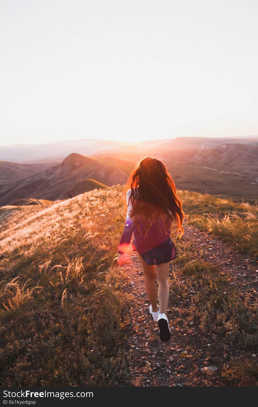 Happy young woman running on feather grass field in sunset light. Nature lifestyle and amazing view around. Long black hair with colored locks. Happy young woman running on feather grass field in sunset light. Nature lifestyle and amazing view around. Long black hair with colored locks