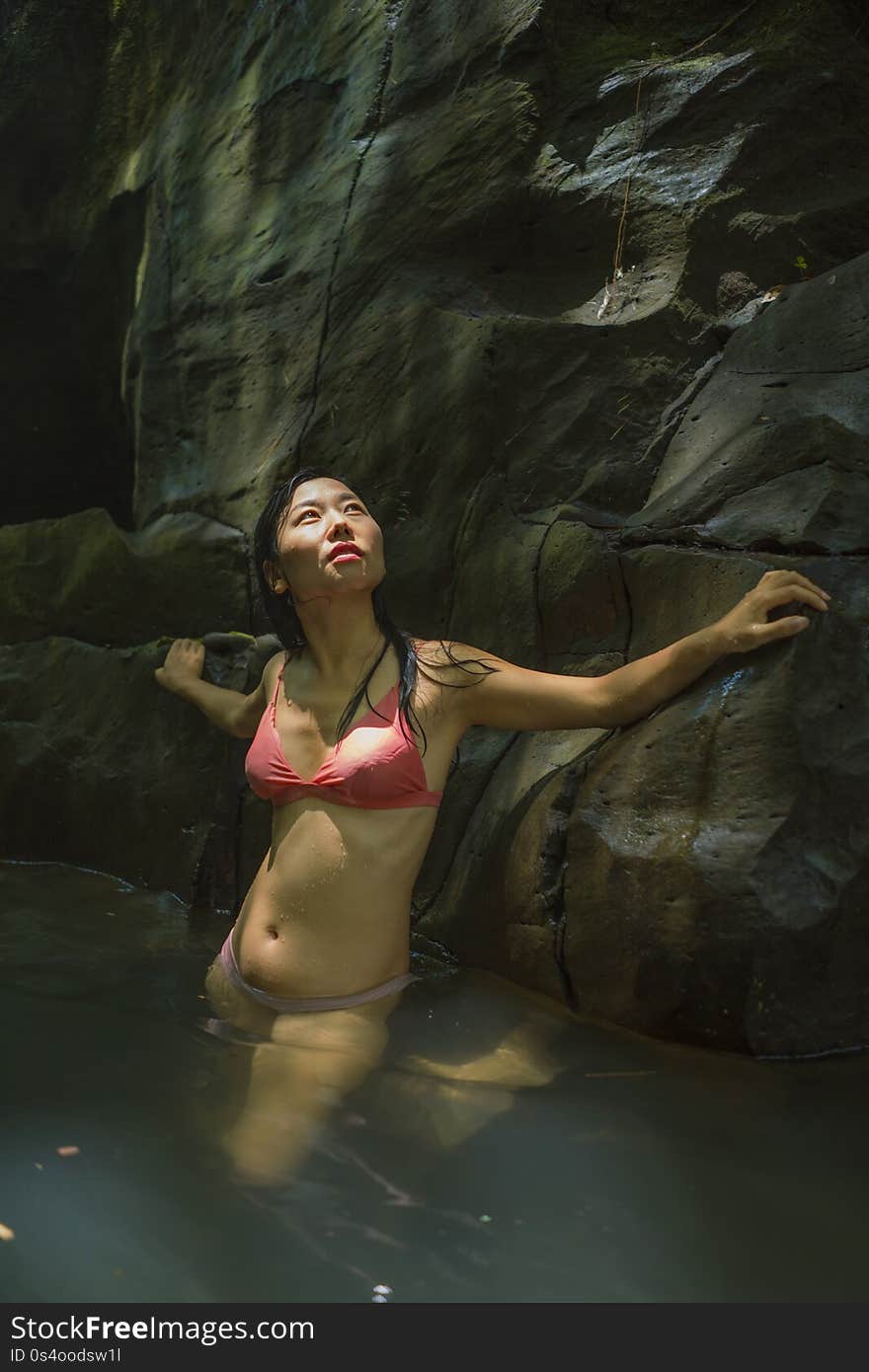 Young beautiful and happy Asian Chinese woman in bikini enjoying unique Summer holidays at tropical forest refreshing relaxed in natural pool delighted by the magical feeling at the jungle lake