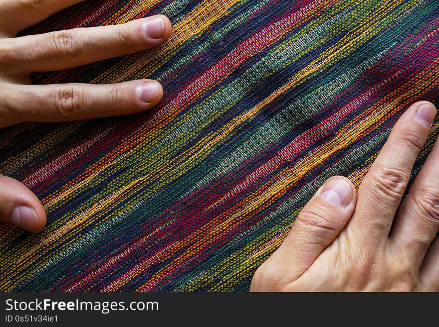 Man hands on motley striped fabric cloth material closeup. Tapestry background top view. Man hands on motley striped fabric cloth material closeup. Tapestry background top view