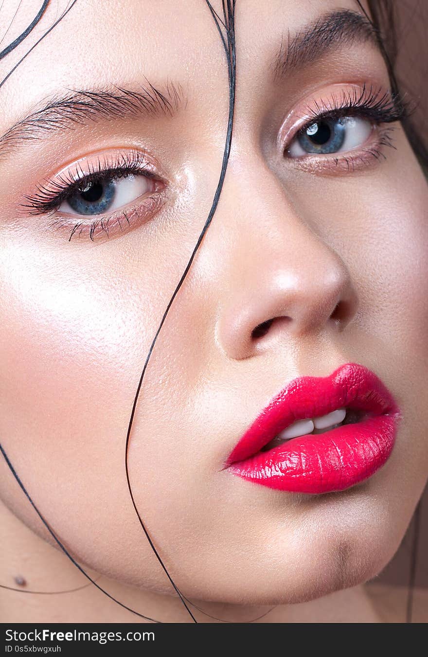 Young model with professional makeup, perfect skin, wet lock on a face. Glossy eyelids and glossy red lips.