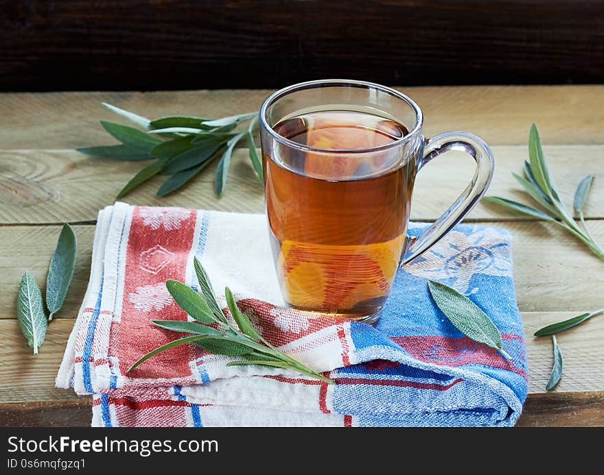 Sage herbal tea or decoction in a glass cup with herb leaves all around on linen blue with red napkin and wooden table, closeup, copy space, alternative medicine and naturopathy concept. Sage herbal tea or decoction in a glass cup with herb leaves all around on linen blue with red napkin and wooden table, closeup, copy space, alternative medicine and naturopathy concept