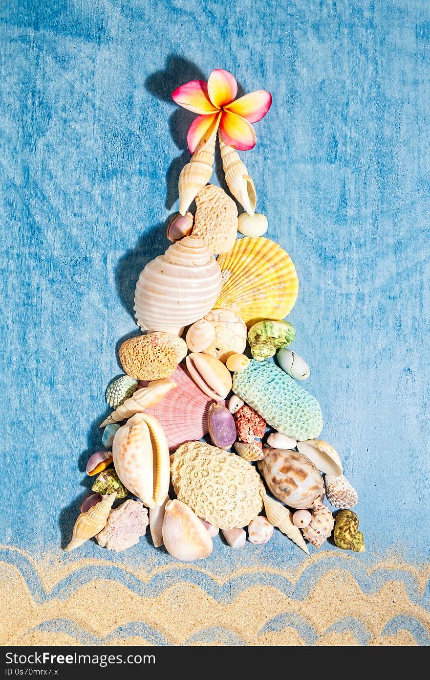 Christmas background with a creative arrangement of seashells, corals and white frangipani flower forming a Xmas tree on blue background, flat lay, vertical composition.