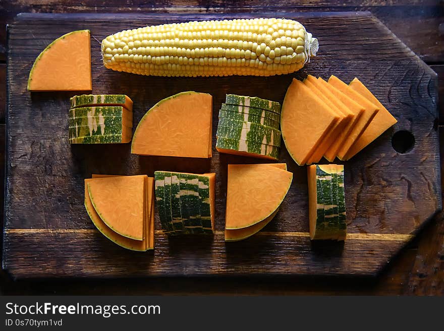 Sliced delicious raw pumpkin and cob of sweet corn on a dark wood board