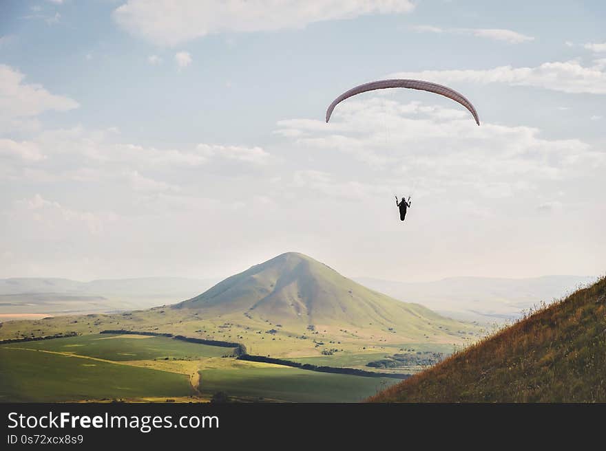 A white-orange paraglider flies over the mountainous terrain.