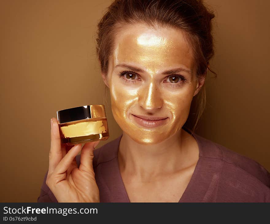 Woman with golden mask showing creme against bronze background