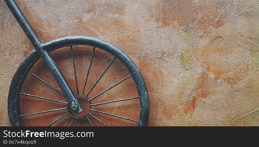Black iron or steel wheel hanging on brown rough wall with right copy space in vintage tone. Part of bicycle made by human for decoration home and Vintage or retro object concept