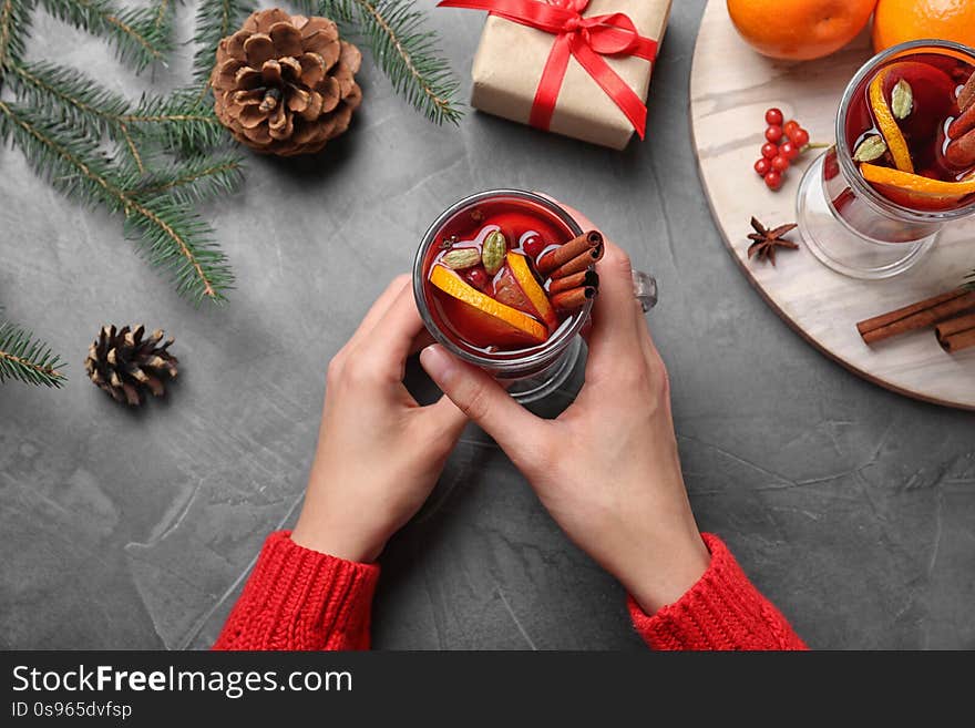 Young woman holding glass of tasty mulled wine at grey table