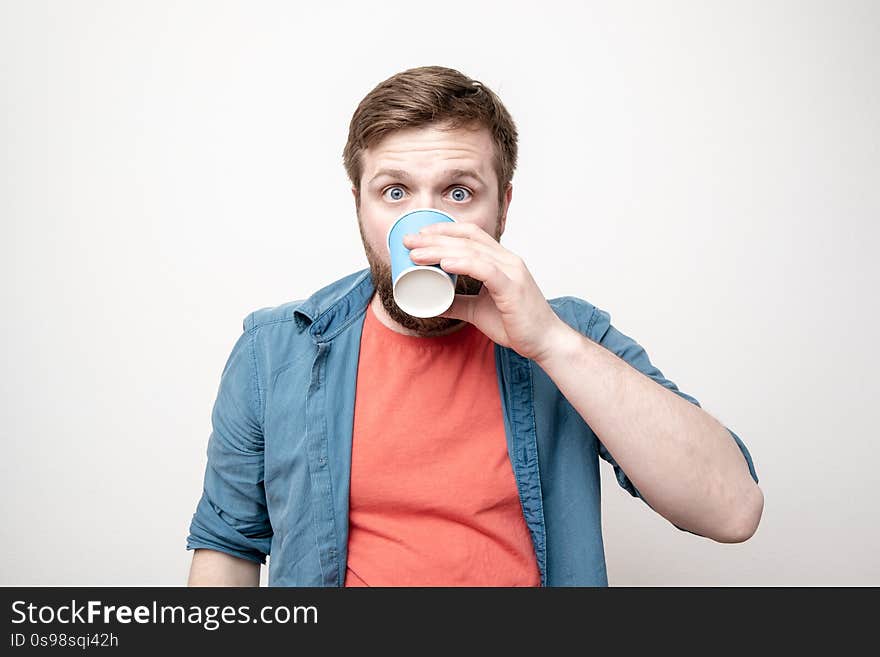 Man with a paper cup in hand, drinks and is shocked by a spoiled drink, his eyes widen and horror appears on face. Negative emotions. Concept of spoiled products. Man with a paper cup in hand, drinks and is shocked by a spoiled drink, his eyes widen and horror appears on face. Negative emotions. Concept of spoiled products