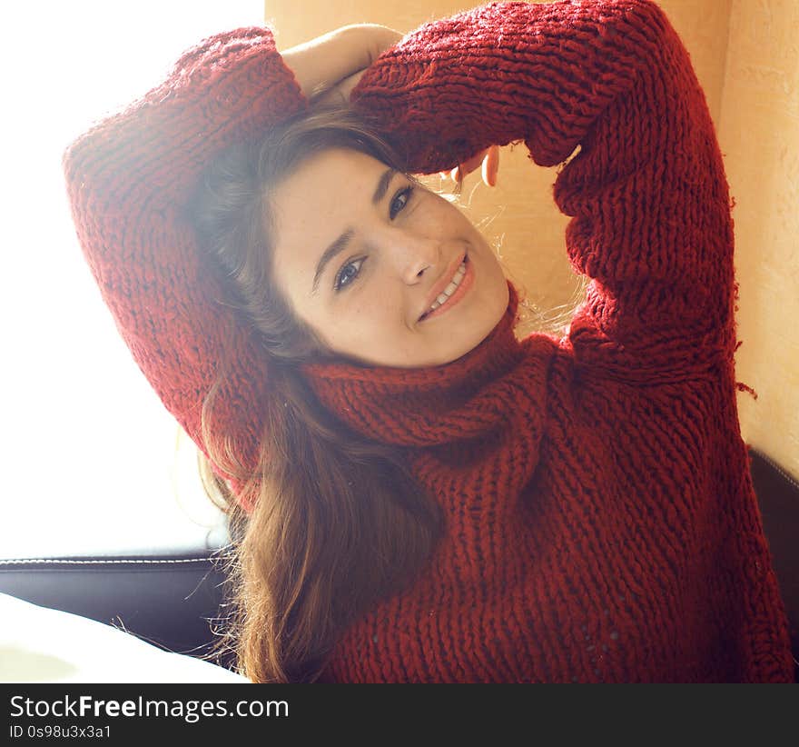 Young pretty real woman in red sweater and scarf all over her face smiling at home, winter positive