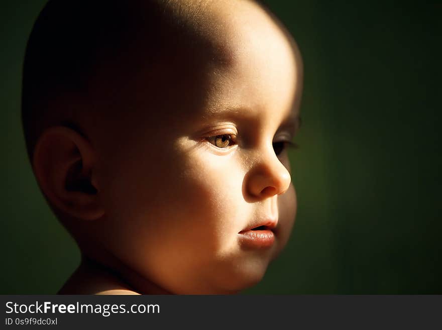 Face of a young child on a green background, rays of the sun.