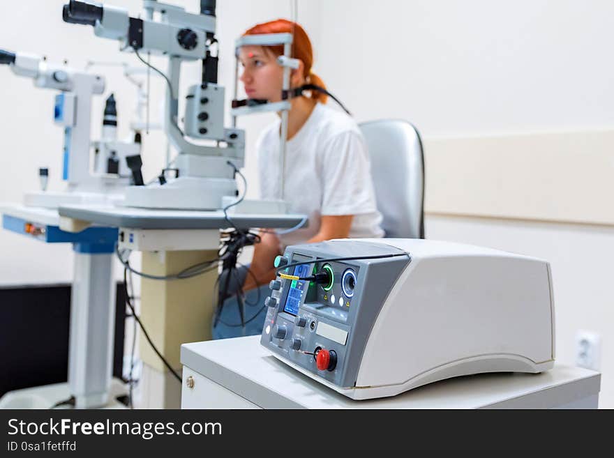 View of red-haired teenager girl in ophthalmologist cabinet getting laser coagulation on modern equipment. View of red-haired teenager girl in ophthalmologist cabinet getting laser coagulation on modern equipment