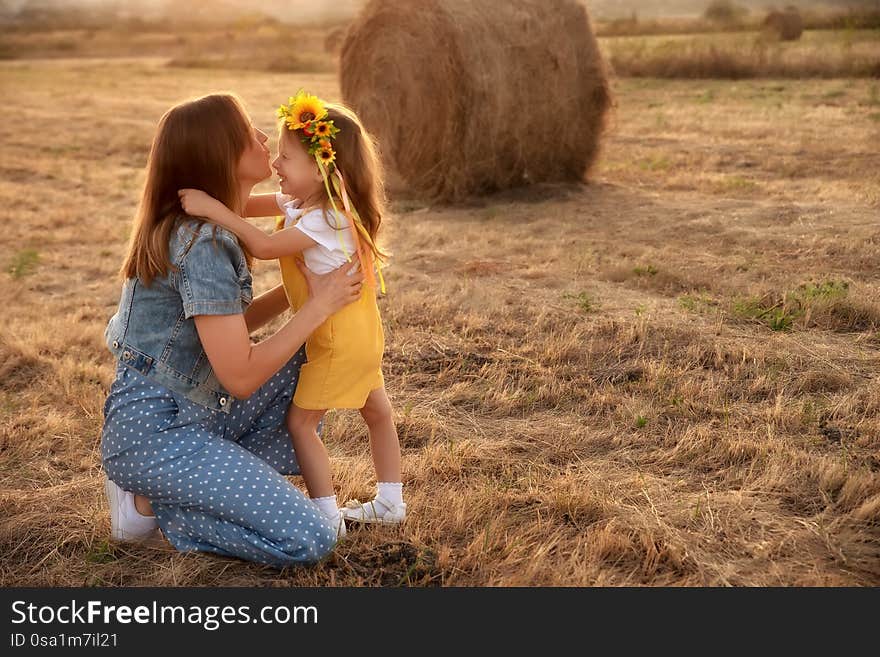 Happy girl child in yellow dress hugs young mom in autumn field