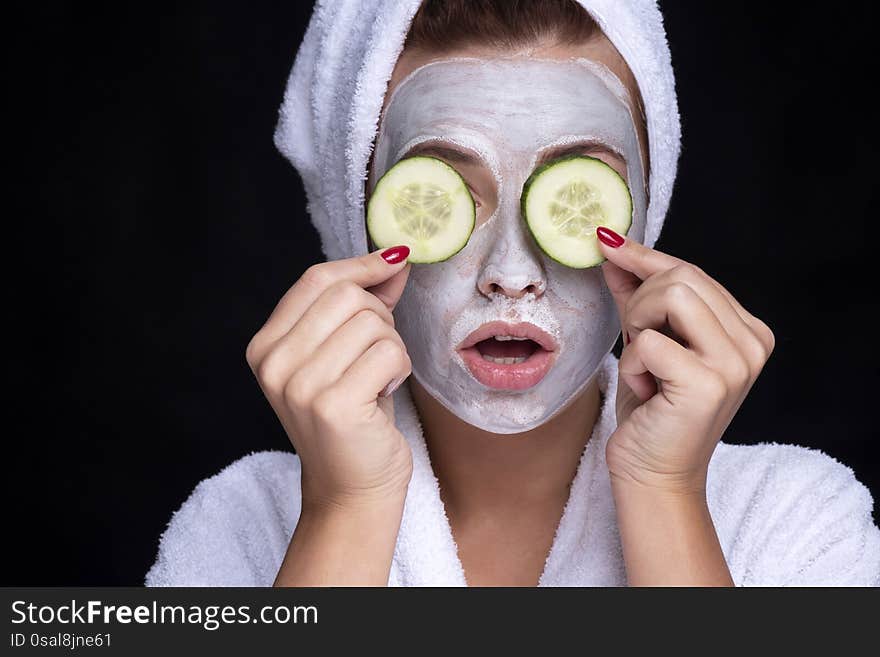 Beautiful young european woman apply clay mask on her face with towel on her head and cucumbers on her eyes. beauty spa concept.