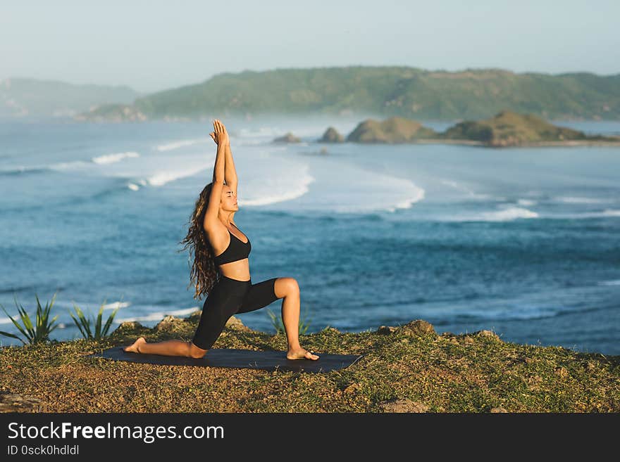 Woman practicing yoga outdoors with amazing ocean and mountain view