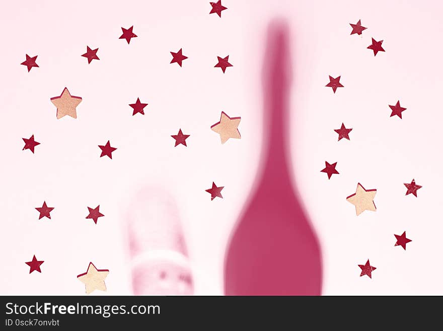 Shadows of champagne bottle and glass with confetti and glitter on pink background. Creative christmas card flat lay