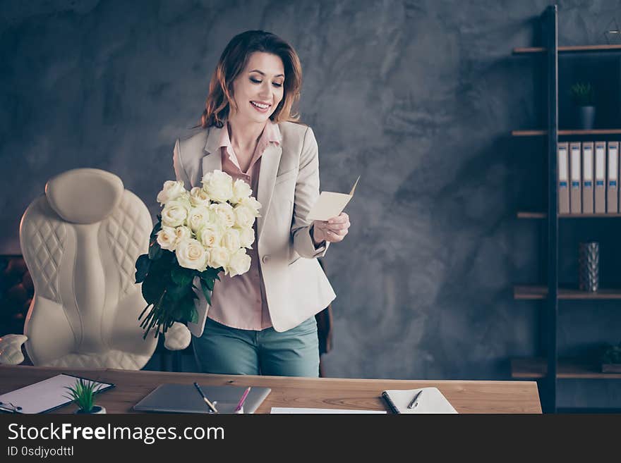 Portrait of her she nice attractive cheerful cheery mature lady holding in hands white roses, reading romance post card professional holiday day at industrial style interior work place station. Portrait of her she nice attractive cheerful cheery mature lady holding in hands white roses, reading romance post card professional holiday day at industrial style interior work place station