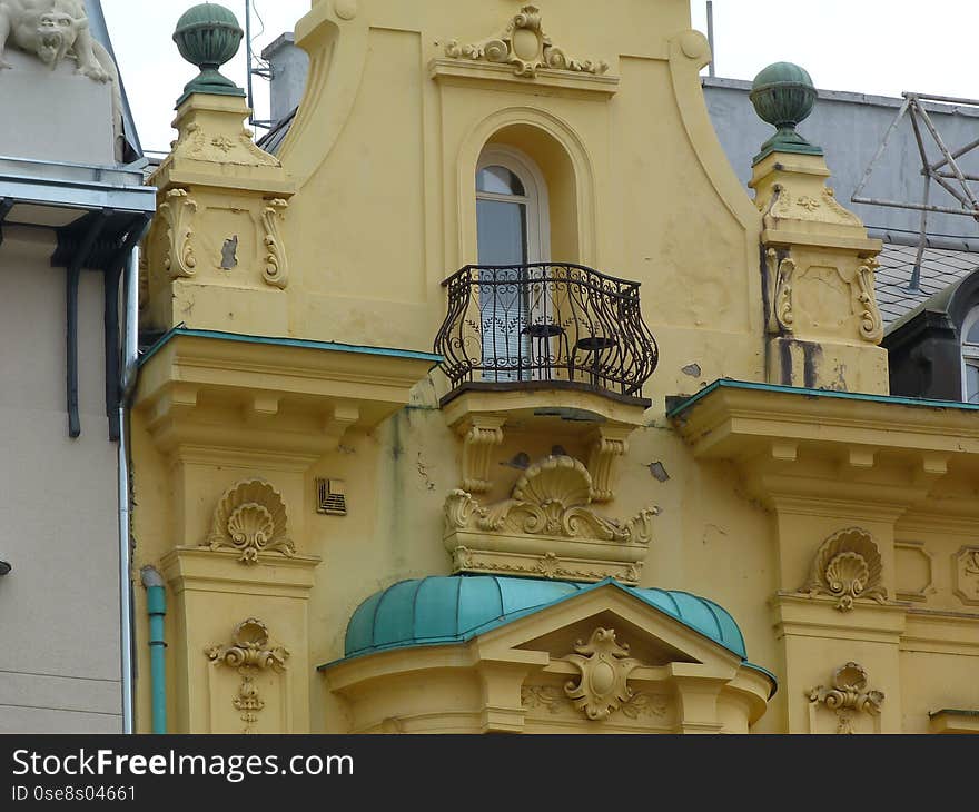 Yellow stucco exterior detail in Baroque stile in downtown Zagreb, Croatia with rich decoration and black wrought iron balcony railing. aged green copper roofing over bay window. tourism concept. Yellow stucco exterior detail in Baroque stile in downtown Zagreb, Croatia with rich decoration and black wrought iron balcony railing. aged green copper roofing over bay window. tourism concept.