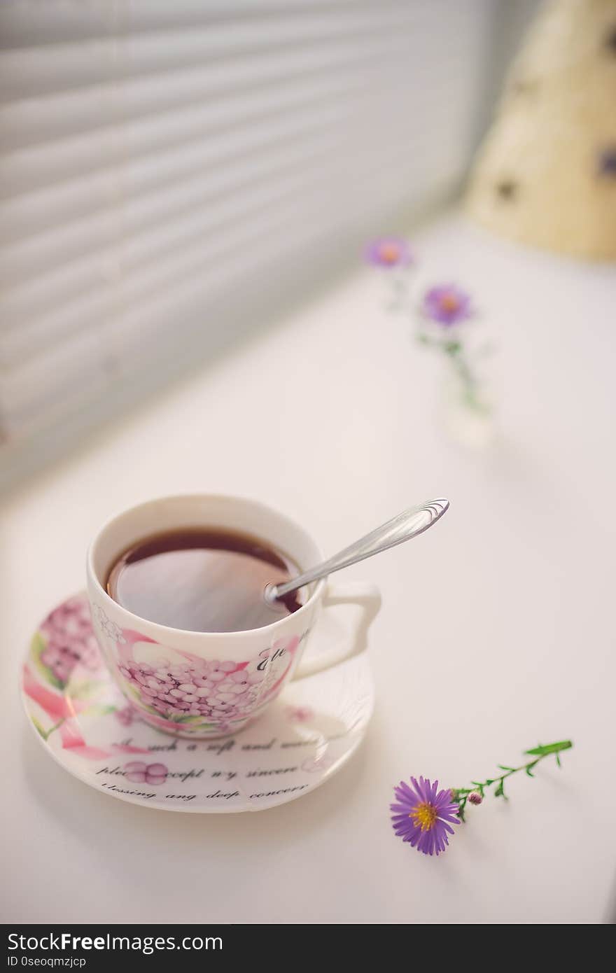 Black tea in an elegant vintage porcelain cup and spoon on the white windowsill.