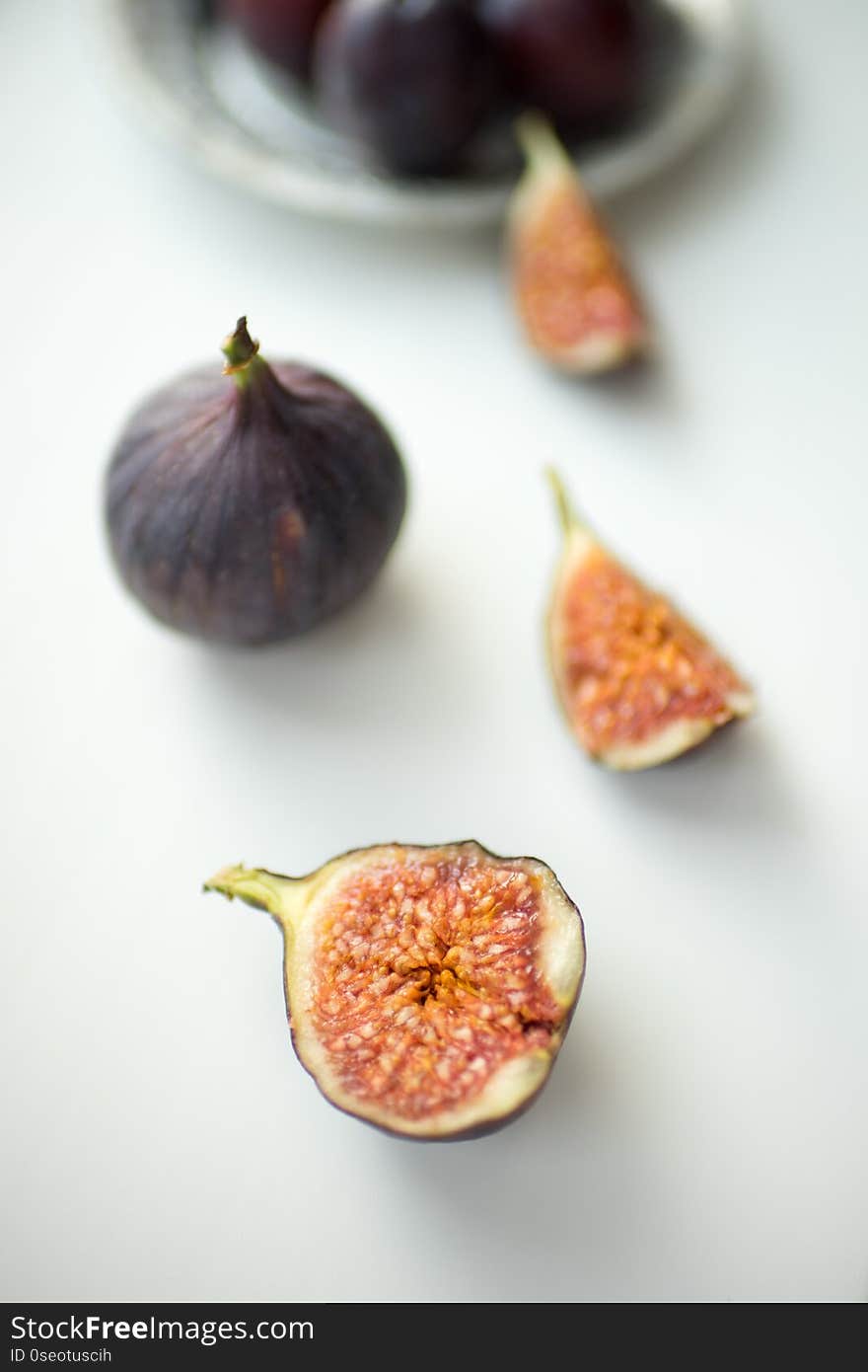 One whole fig and the other sliced lie on a white table.