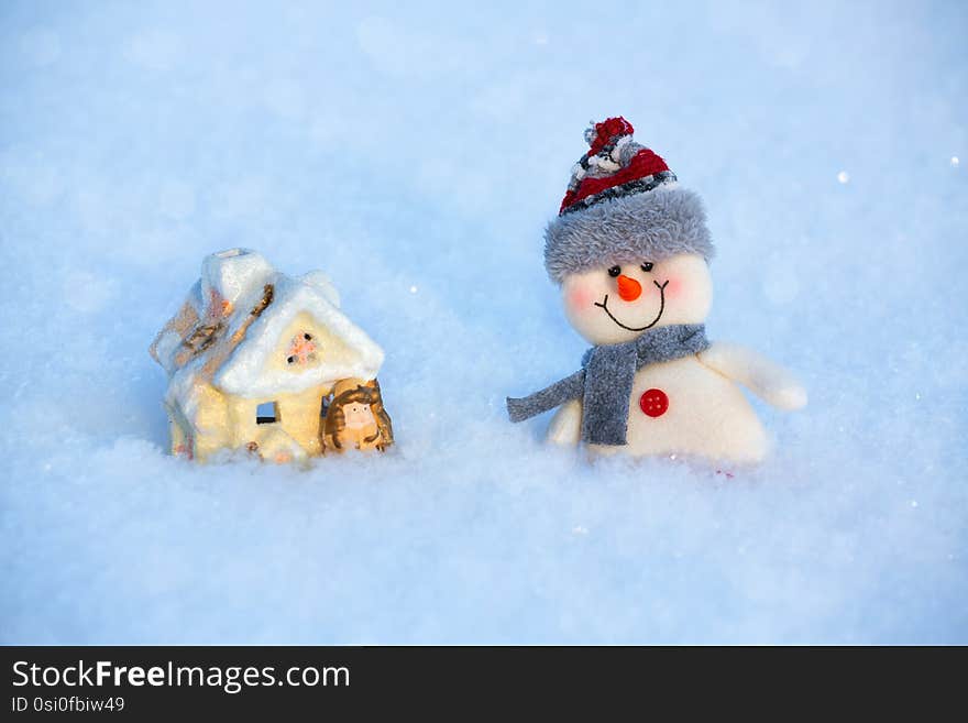 On the snow is a happy funny toy snowman and toy house. The snowman is wearing a fur hat and scarf. The concept of winter, Christmas, New year. Copy space. horizontal orientation. On the snow is a happy funny toy snowman and toy house. The snowman is wearing a fur hat and scarf. The concept of winter, Christmas, New year. Copy space. horizontal orientation.