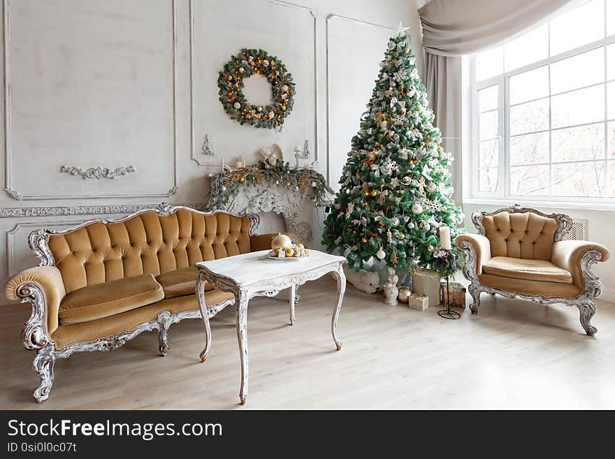 Christmas morning in classic apartments with a white fireplace, decorated tree, sofa, large windows and chandelier.