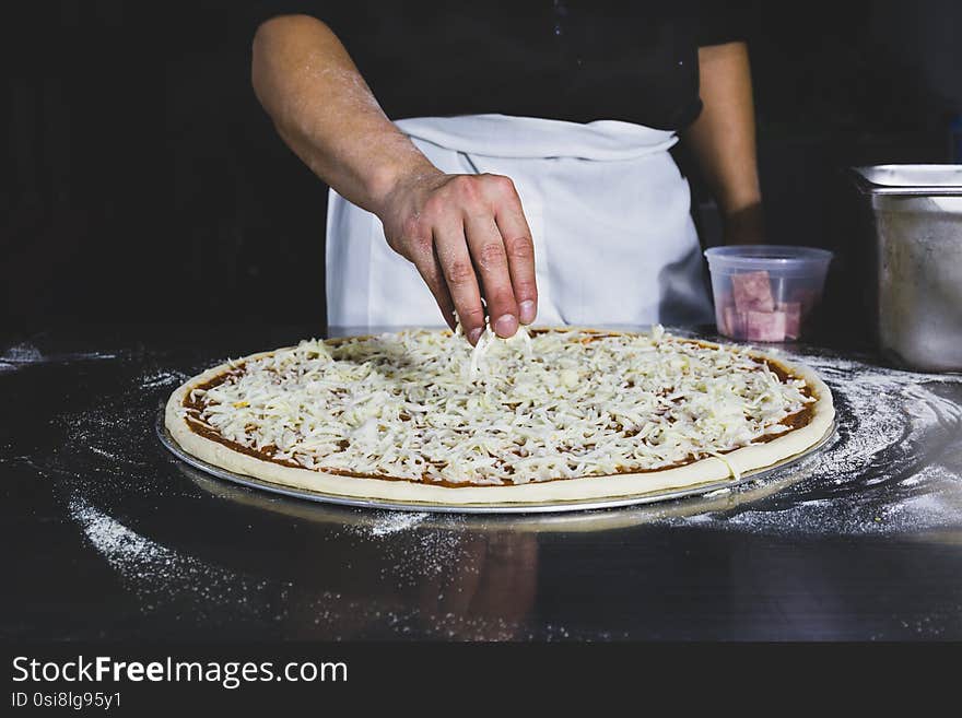 Chefs hand putting cheese on the pizza in black background.