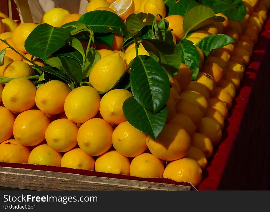 Fresh bright yellow lemons and green leaves on display at market place on old wooden table in bright sunlight with strong shadows. organic and healthy food concept.