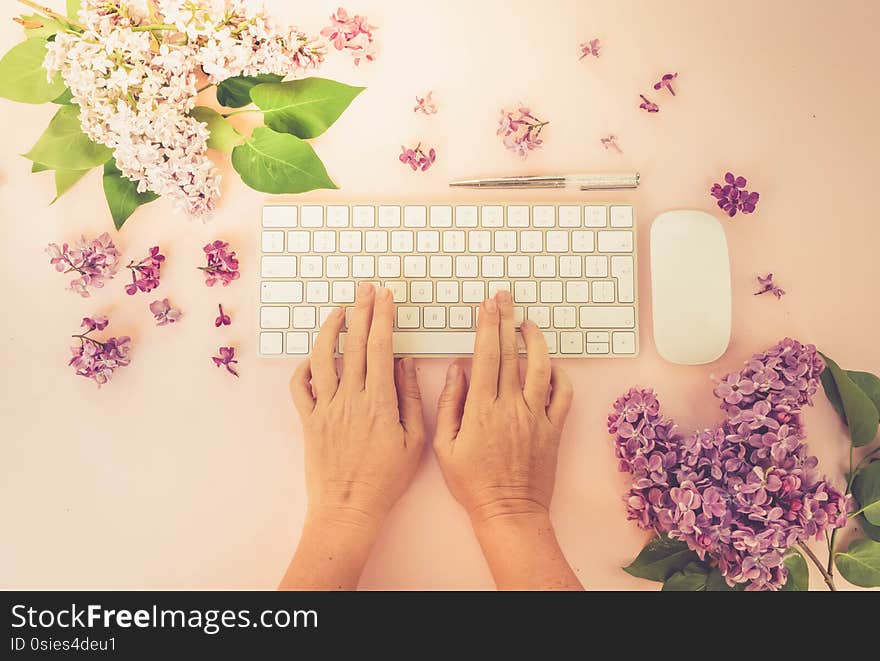 Flat lay home office workspace - modern keyboard with two hands typing, fresh lilac flowers, toned. Flat lay home office workspace - modern keyboard with two hands typing, fresh lilac flowers, toned