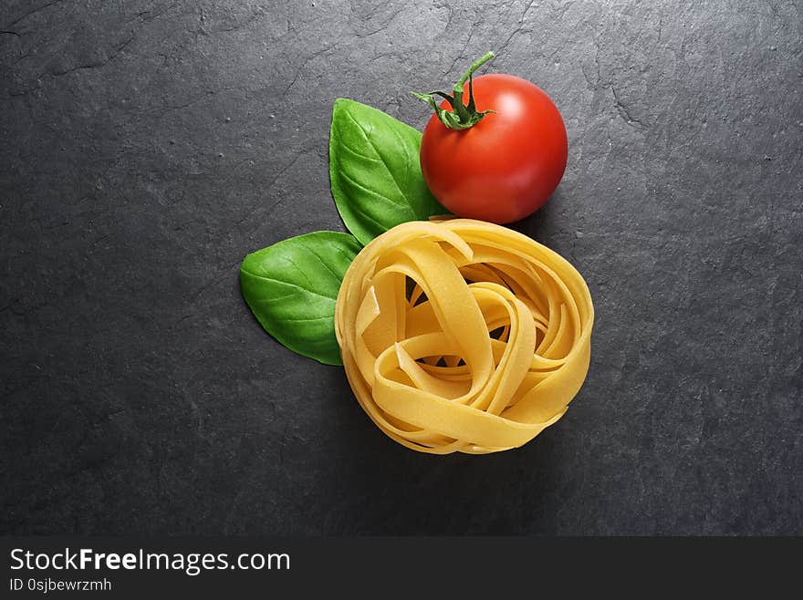 Fettuccine pasta with basil leaves and tomato on black slate background with copy space. Fettuccine pasta with basil leaves and tomato on black slate background with copy space