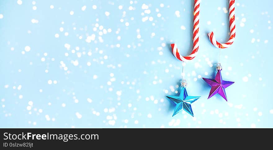 Two candy canes with toys on the Christmas tree in the form of stars on a blue background. Banner for the site. Two candy canes with toys on the Christmas tree in the form of stars on a blue background. Banner for the site.