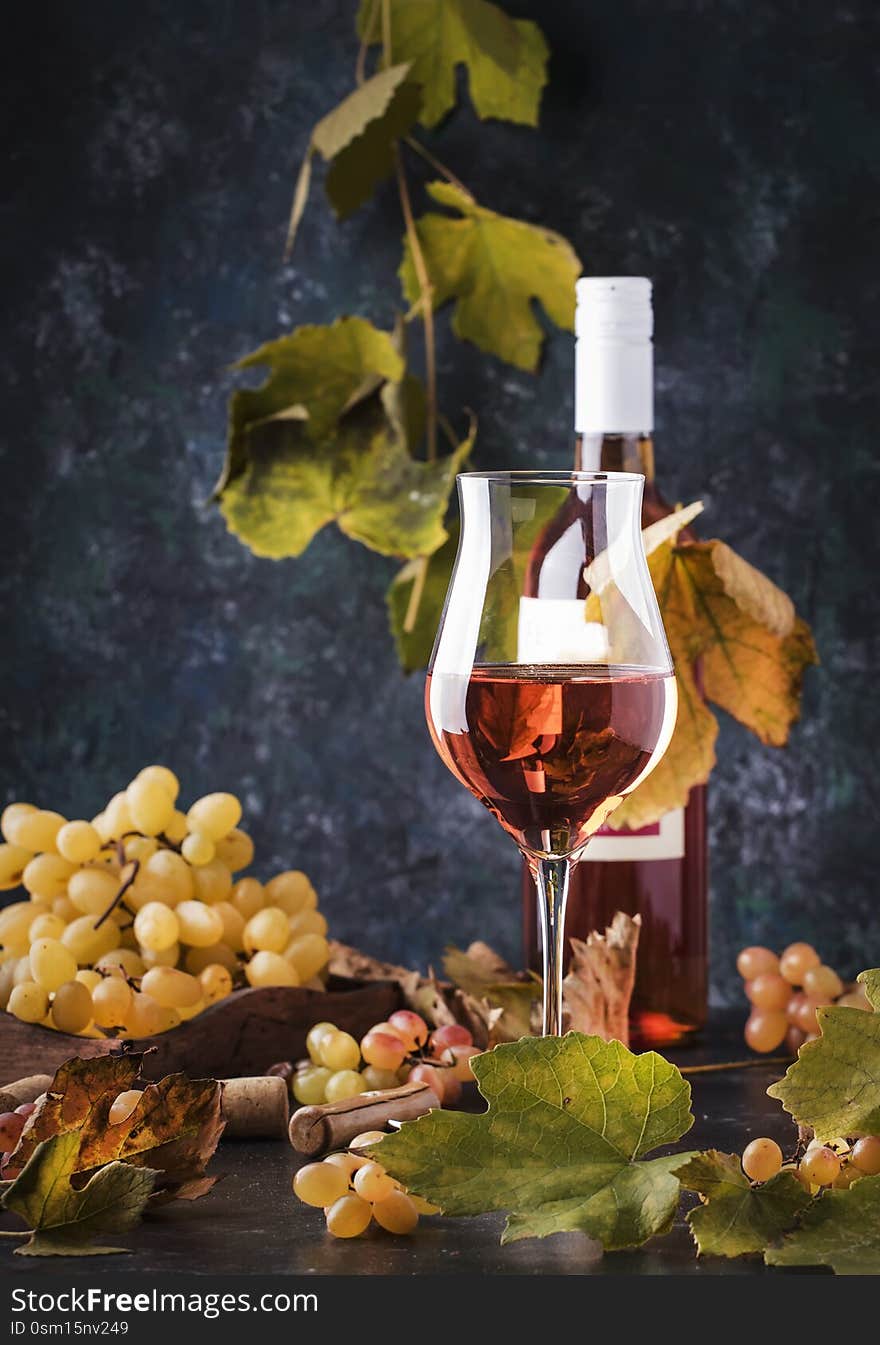 Rose wine at wine tasting concept. Gray background with grape and leaves. Pink wine in wineglass. Copy space