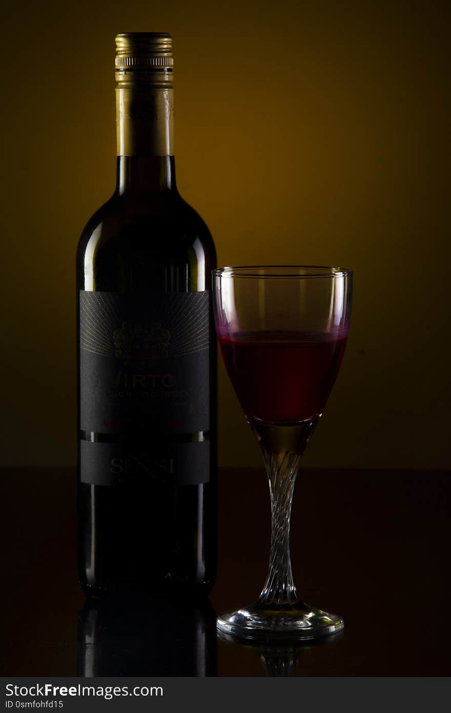 A glass and a bottle of wine on the table under low key light. A glass and a bottle of wine on the table under low key light