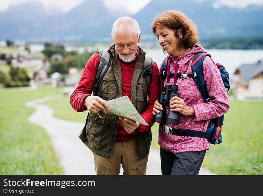 Senior pensioner couple with hiking in nature, using binoculars and map.