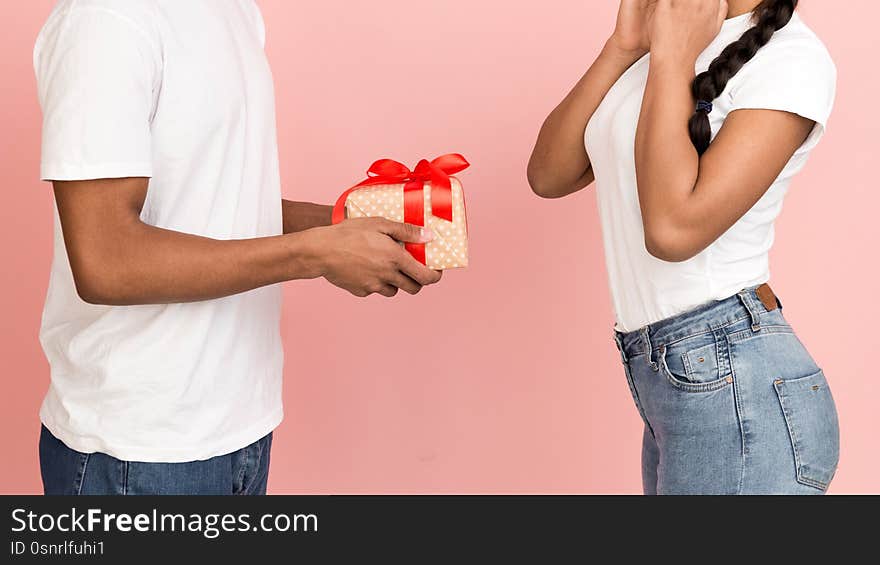 Romantic surprise. Guy giving present to his girlfriend over pink background, crop