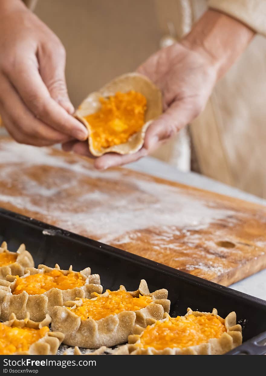 Stage of preparation of Karelian pies. Pies are located on a baking sheet, ready for baking. In the background, a woman is