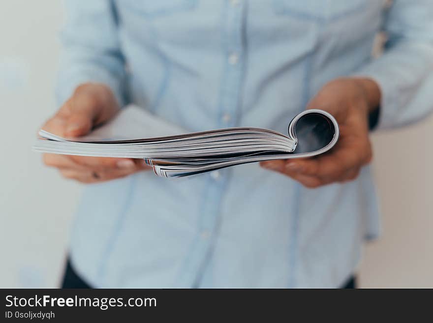 Beautiful female hands are holding an open book or magazine in a room on against a light wall. Beautiful female hands are holding an open book or magazine in a room on against a light wall