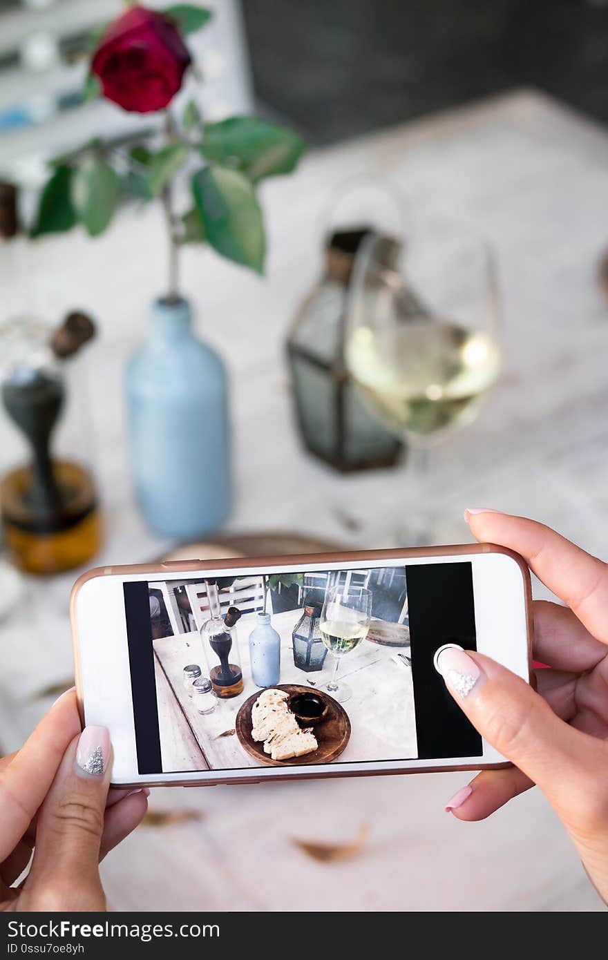 Woman taking photo of bread and wine on her smartphone in restaurant. Bali.