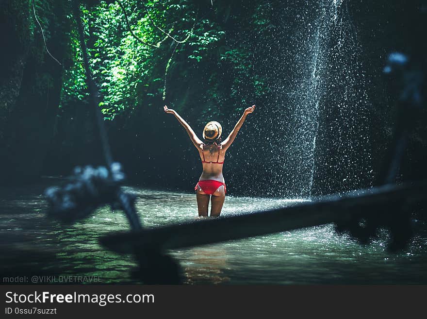 Young woman tourist with straw hat deep in the rainforest with waterfall background. Bali island. Indonesia.