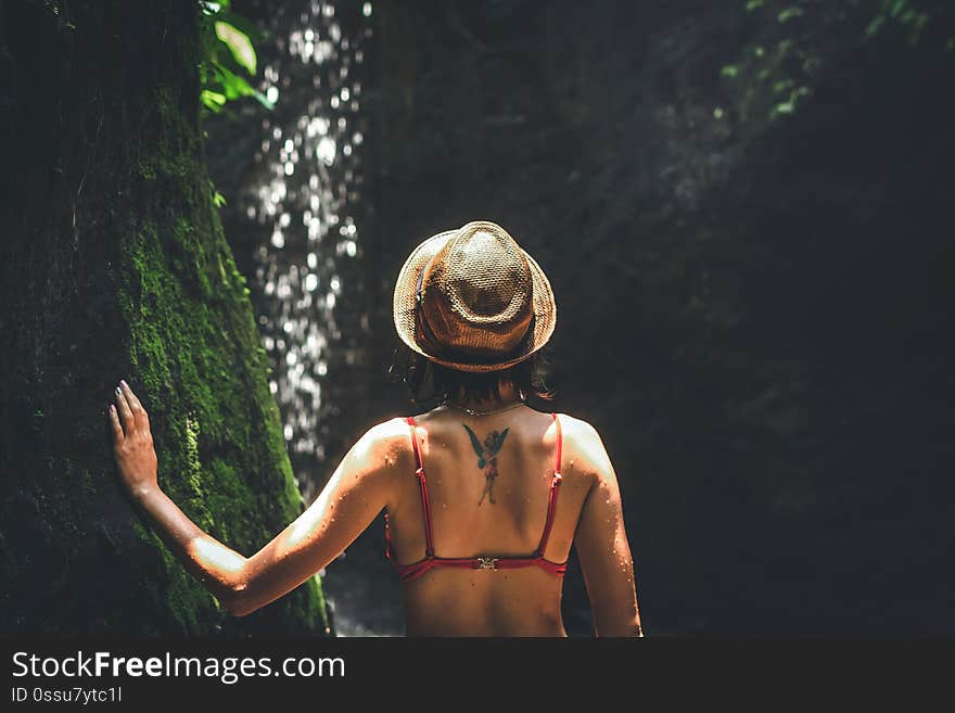 Young woman tourist with straw hat deep in the rainforest with waterfall background. Bali island. Indonesia.