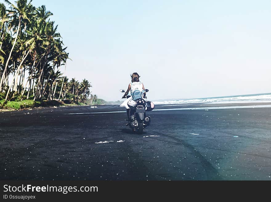 Young woman driving a scooter at the beach with black sand. Bali island. Indonesia.