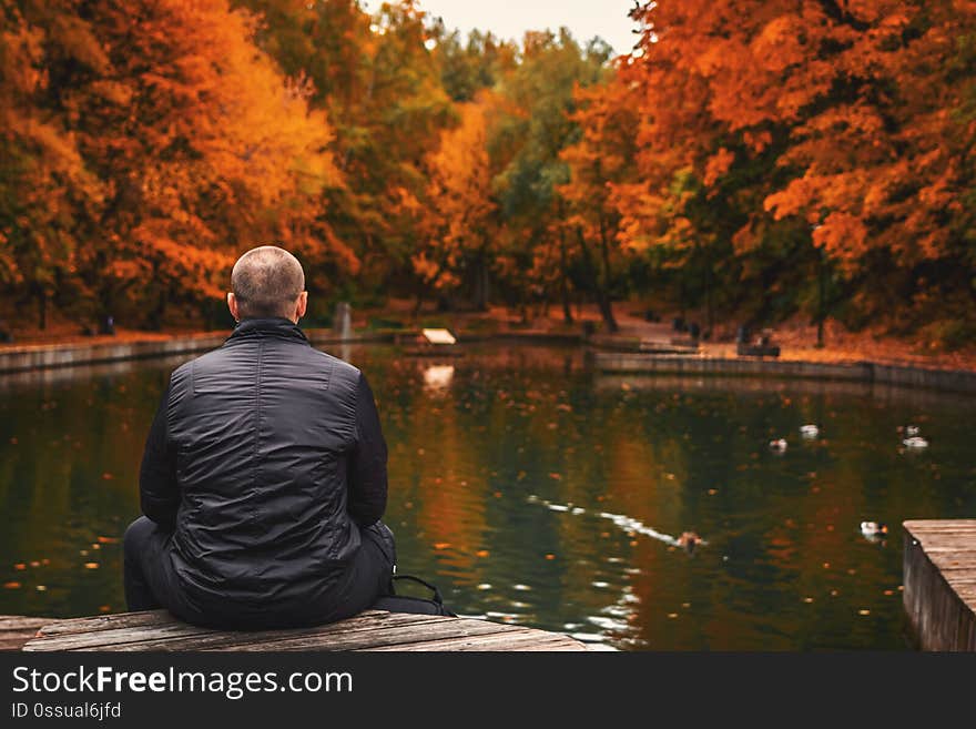 Alone man sits beside a pond in the park. Autumn background.