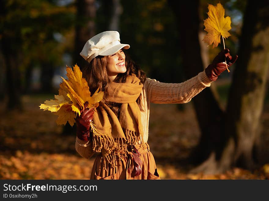 Happy woman outside in autumn park looking at yellow leaf